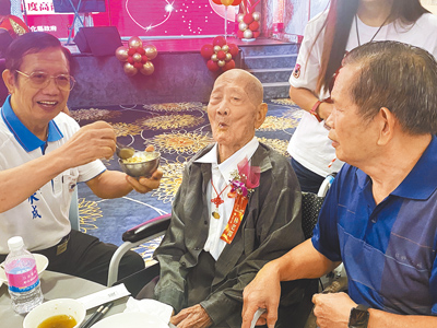 104歲人瑞林老闖(中)參加彰化高齡同學會,兒子林水成(左)表示,會把父親愛吃的魚肉弄碎拌在飯裡,他一天能吃8碗飯。(葉靜美攝) image