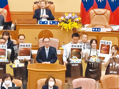 民進黨議員10日市政總質詢響應新北市長侯友宜(站備詢台者)先前赴美稱「失業賣漢堡」一說,端出象徵國民黨主席朱立倫和下屆市長熱門人選的「烤豬漢堡」、「蔥味漢堡」、「四川漢堡」、「荷蘭漢堡」要侯友宜選,侯笑回「怎麼這麼關心國民黨、民眾黨的事情勒,關心市政才是關心新北市」。(柯毓庭攝) image
